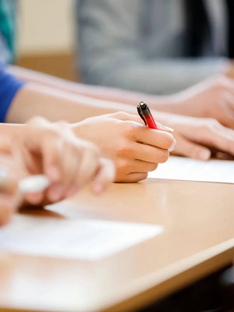 Multiple student's hands writing on a desk.